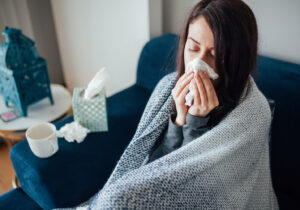 Sick woman blowing her nose, she covered with blanket