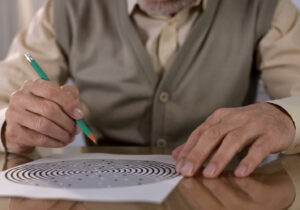 Concentrated retired man solving logic test at table, memory exercise, neurology